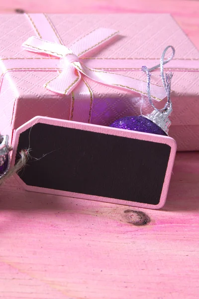 Tarjeta de Navidad con etiqueta, caja de regalo y bolas de Navidad sobre fondo rosa — Foto de Stock