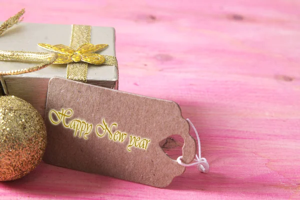 Felice anno nuovo biglietto con confezione regalo e tag su bakckground in legno rosa — Foto Stock