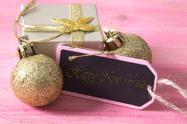 Kerstkaart met label, doos van de gift en kerstballen op roze achtergrond — Stockfoto