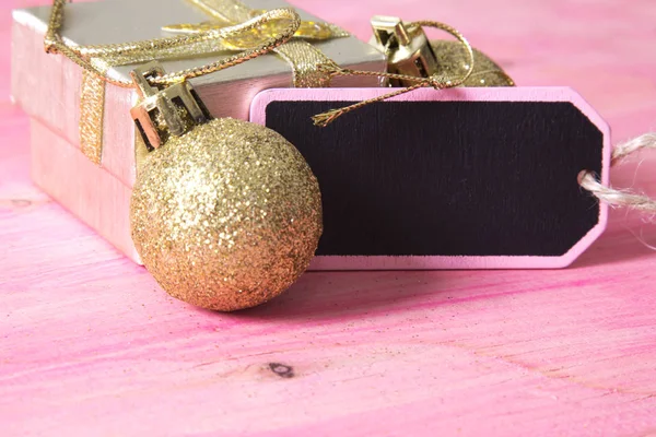 Cartão de Natal com etiqueta, caixa de presente e bolas de Natal no fundo rosa — Fotografia de Stock