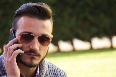 Parkta cep telefonunda konuşan genç hipster adam