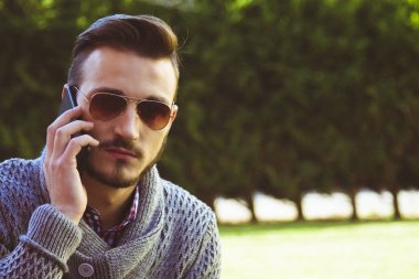 Parkta cep telefonunda konuşan genç hipster adam