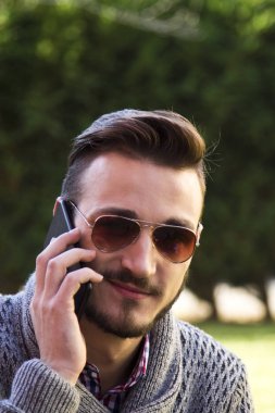Parkta cep telefonunda konuşan genç hipster adam