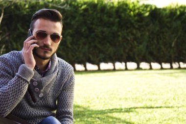Parkta cep telefonunda konuşan genç hipster adam