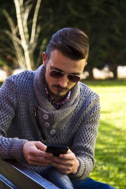Parkta cep telefonu kullanan genç hipster adam