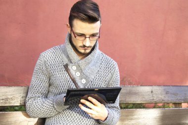 tablet kullanarak arka planda pembe duvar ile parkta oturan genç adam