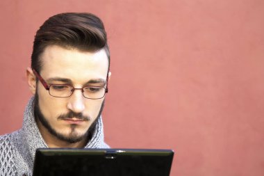 tablet kullanarak arka planda pembe duvar ile parkta oturan genç adam