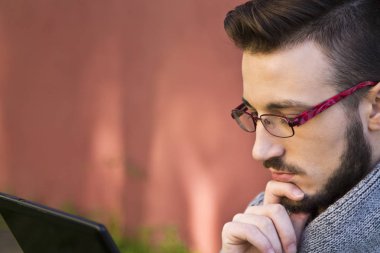 tablet kullanarak arka planda pembe duvar ile parkta oturan genç adam