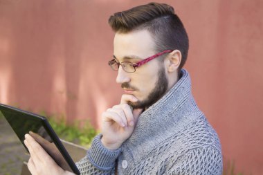 tablet kullanarak arka planda pembe duvar ile parkta oturan genç adam