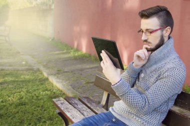 tablet kullanarak arka planda pembe duvar ile parkta oturan genç adam