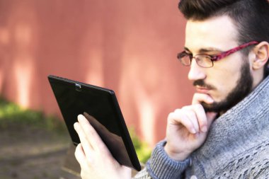 tablet kullanarak arka planda pembe duvar ile parkta oturan genç adam