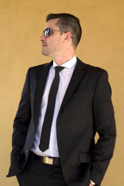 Takım elbiseli, elleri ceplerinde bir adam.
