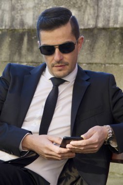Cep telefonu kullaranarak parkta oturan takım elbiseli genç adam