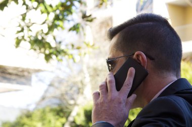 Cep telefonu ile konuşurken parkta oturan takım elbiseli genç adam