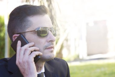 Cep telefonu ile konuşurken parkta oturan takım elbiseli genç adam