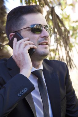 Cep telefonu ile konuşurken parkta oturan takım elbiseli genç adam