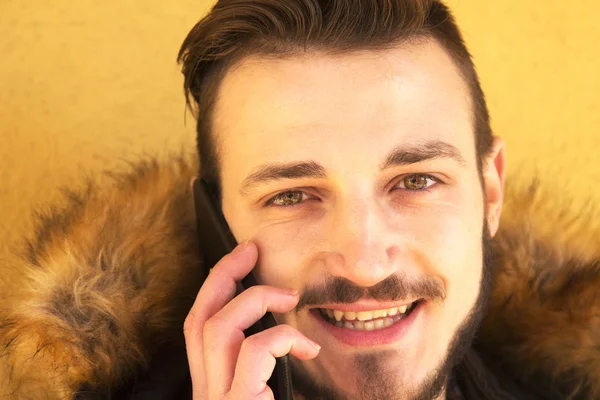 Чоловік молодий розмовляє з мобільним телефоном підтримується на стіні жовтим — стокове фото