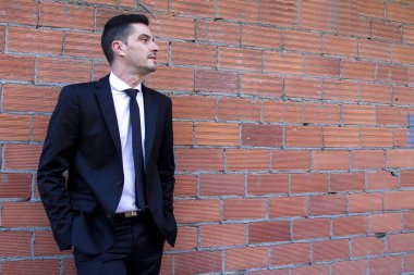 Takım elbiseli, elleri ceplerinde bir adam.