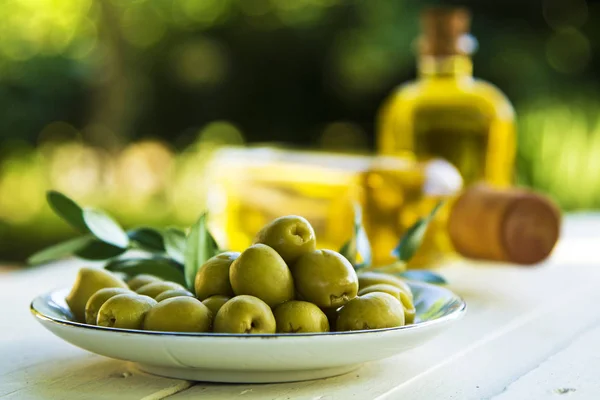 Тарелка оливок и бутылки оливкового масла на столе — стоковое фото