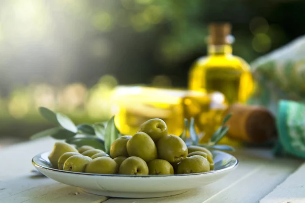 Тарелка оливок и бутылки оливкового масла на столе — стоковое фото