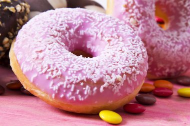 Ürün çeşitliliği ile şeker pembe ahşap arka plan üzerinde renkli donut