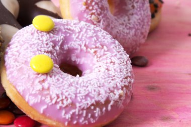 Ürün çeşitliliği ile şeker pembe ahşap arka plan üzerinde renkli donut