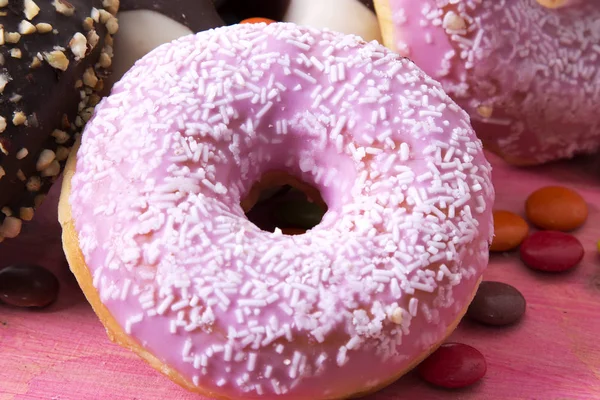 Sortiment av färgglada donuts med godis på rosa trä bakgrund — Stockfoto