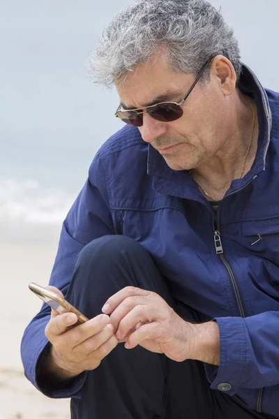 Hombre mayor usando celular en la playa — Foto de Stock