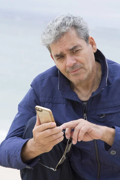Старший чоловік використовує мобільний телефон на пляжі — стокове фото