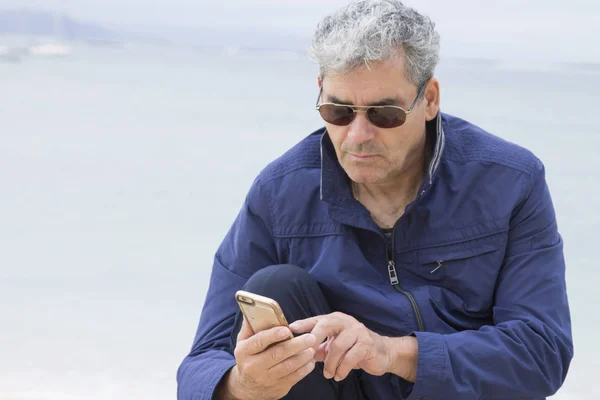 Homem sênior usando celular na praia — Fotografia de Stock