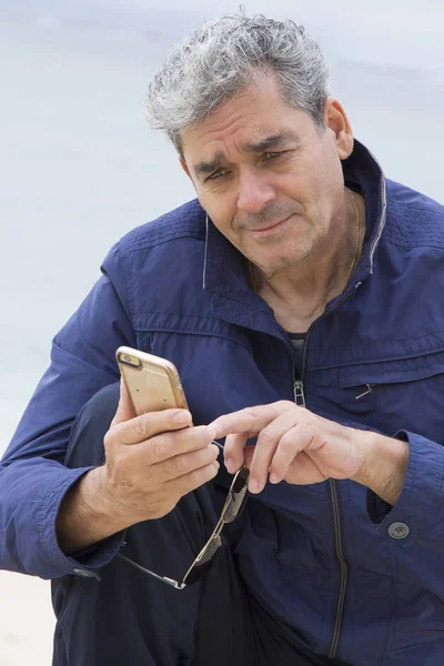 Hombre mayor usando celular en la playa — Foto de Stock