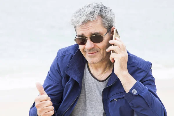 Hombre mayor hablando por teléfono en la playa haciendo señal de ok — Foto de Stock