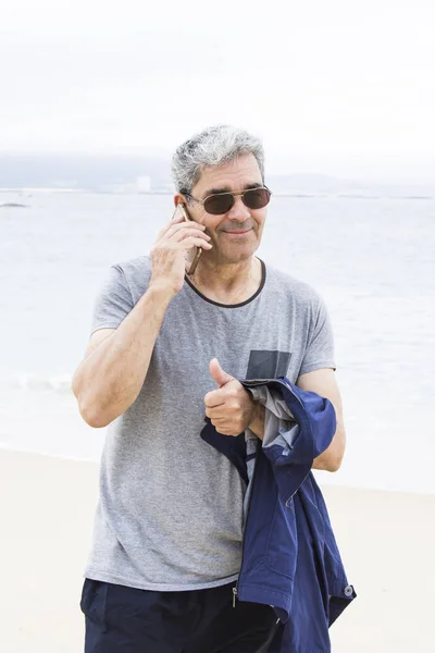 年配の男性がビーチで電話で話しています。 — ストック写真