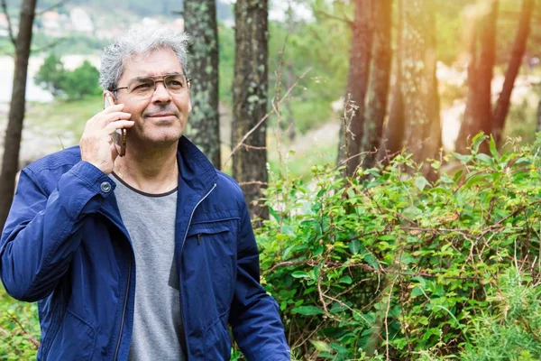 Hombre mayor hablando por celular en el bosque — Foto de Stock