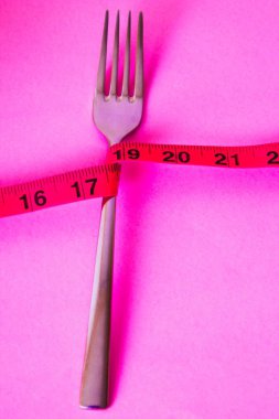düğümlü çatal mezura pembe bir arka plan, diyet ve zayıflama kavramı ile