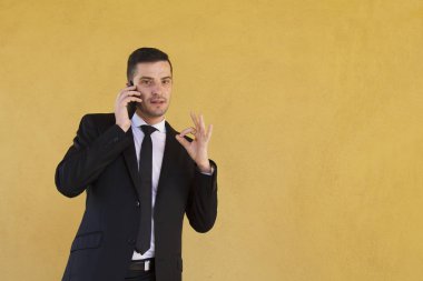Ok işareti yapmak ve cep telefonu ile konuşurken takım elbiseli adam