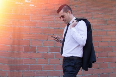 Erkek takım elbise ve cep telefonuyla tuğla zemin üzerine güneş gözlüğü
