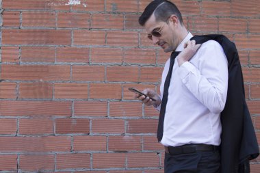 Erkek takım elbise ve cep telefonuyla tuğla zemin üzerine güneş gözlüğü