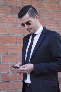 Erkek takım elbise ve cep telefonuyla tuğla zemin üzerine güneş gözlüğü