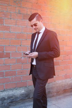 Erkek takım elbise ve cep telefonuyla tuğla zemin üzerine güneş gözlüğü