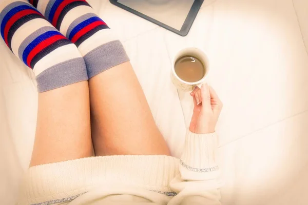 一杯のコーヒーとタブレットを見てベッドの上にソックスの女 — ストック写真