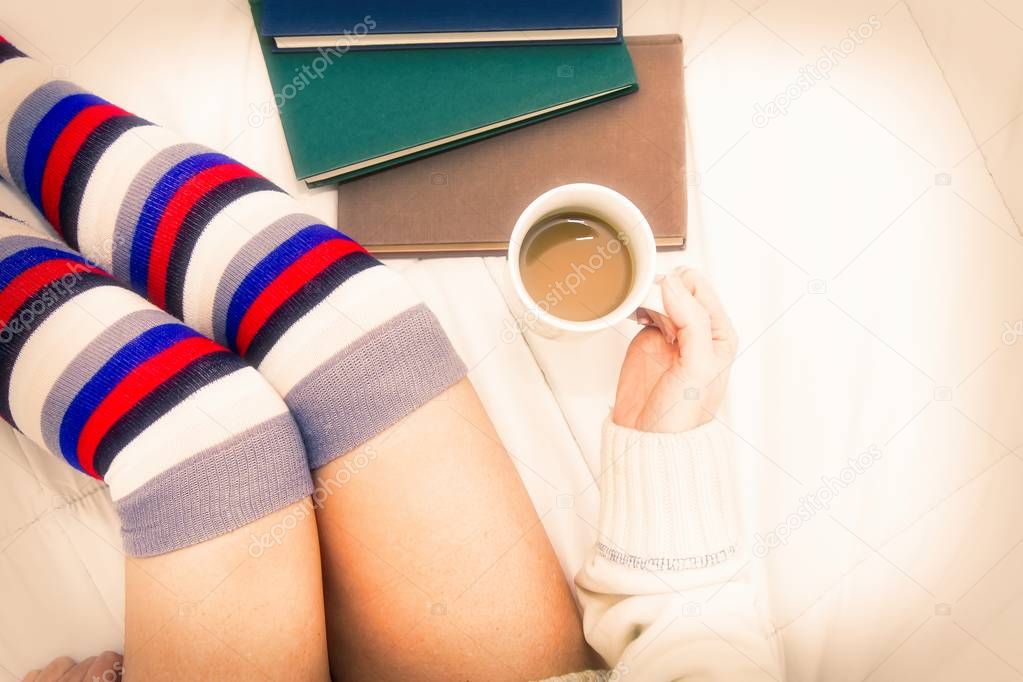 woman in socks on top of the bed with a cup of coffee and some books
