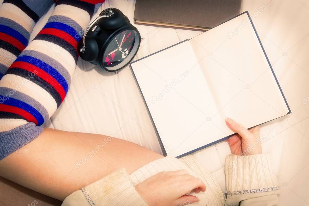 woman in wool socks on the bed with an alarm clock in her hand and some books