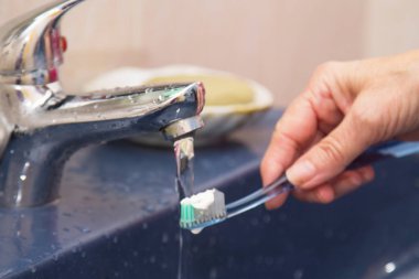 Kadın eli, diş fırçası ve diş macunu banyoda.