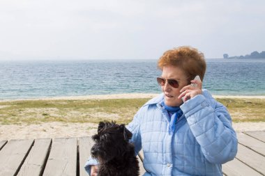 Dışarıda cep telefonu kullanan köpekli yaşlı bir kadın.