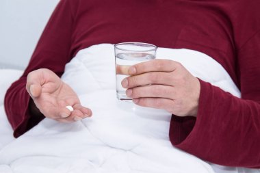 Hasta adam yatağında elinde bir bardak su ve hap tutuyor.