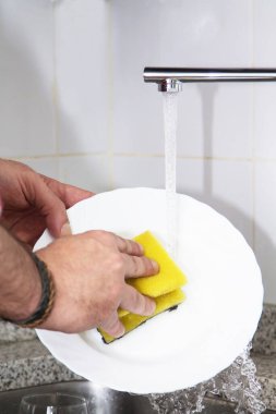 Adam mutfaktaki lavaboda bulaşık yıkıyor.