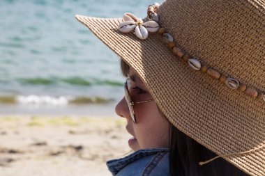 Plajda oturan şapkalı kız denize bakıyor, tatil kavramı, yaz tatili ve rahatlama.