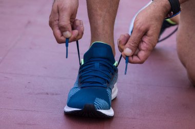 Spor salonunda spor ayakkabı bağlayan bir adam.