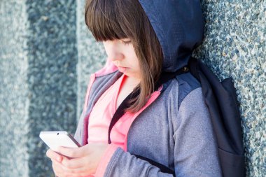 Kız cep telefonuyla duvara yaslanıyor.